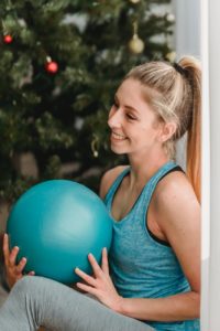 Une femme avec un ballon de gym se tient près du sapin de Noël.